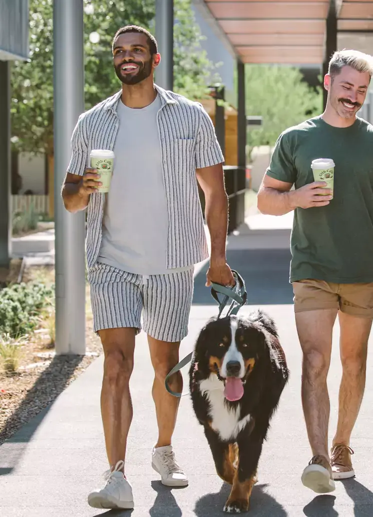 Two guys walking a dog drinking coffee 