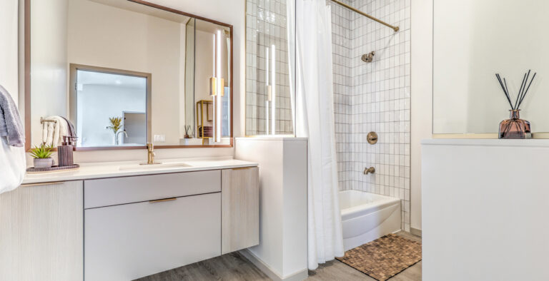 Luxury Apartments For Rent in Las Vegas, NV - Vestra at Uncommons - Bathroom with Tiled Shower and Tub, Luxury Vanity, and Wood-Rimmed Mirror