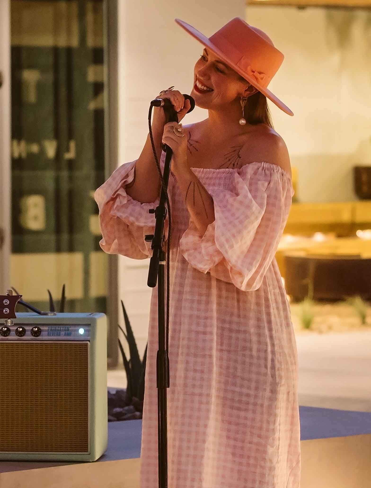 A women in a pink checked dress and cowboy had sings into a microphone